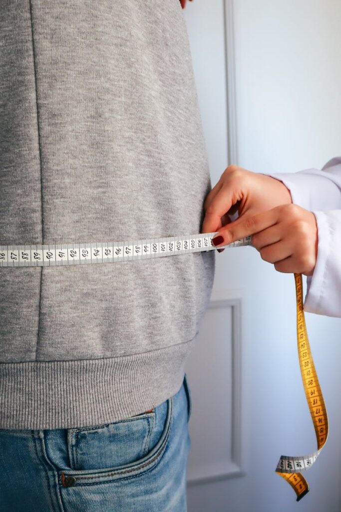 A nutritionist measuring a patient's waist using a tape in a clinical setting.